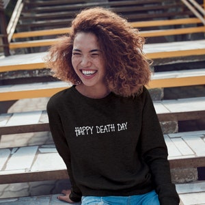May include: A black long-sleeved sweatshirt with the text "HAPPY DEATH DAY" printed in white on the front.