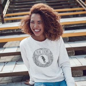 May include: A white sweatshirt with a black and white graphic of a crow with the text "Deaf Crows" on the front.