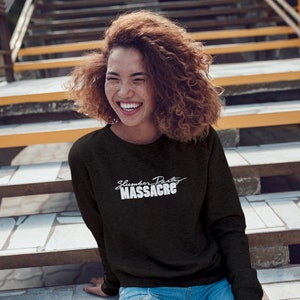 May include: A woman wearing a black long-sleeved sweatshirt with the text "Slumber Party Massacre" in white lettering. She is smiling and sitting on a set of stairs.