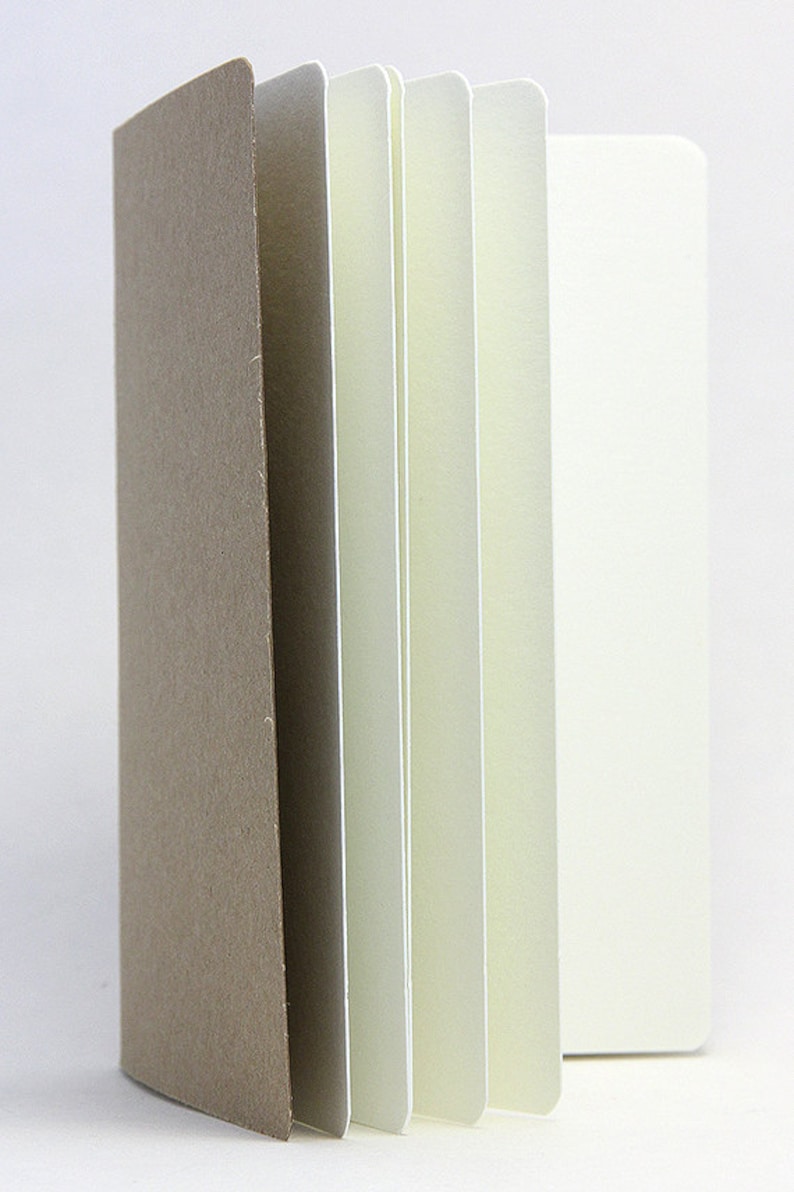 May include: A brown paper covered notebook with white pages. The notebook is closed and the pages are fanned out.