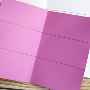 May include: A pink notebook with black lines dividing the pages into sections.