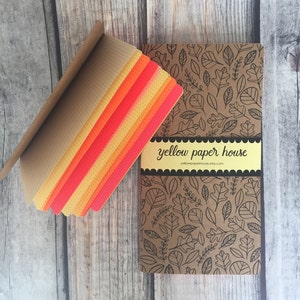 May include: A stack of colorful patterned paper with a brown cover. The cover has a black and white leaf pattern and the text "yellow paper house" with the website address "yellowpaperhouse.etsy.com".