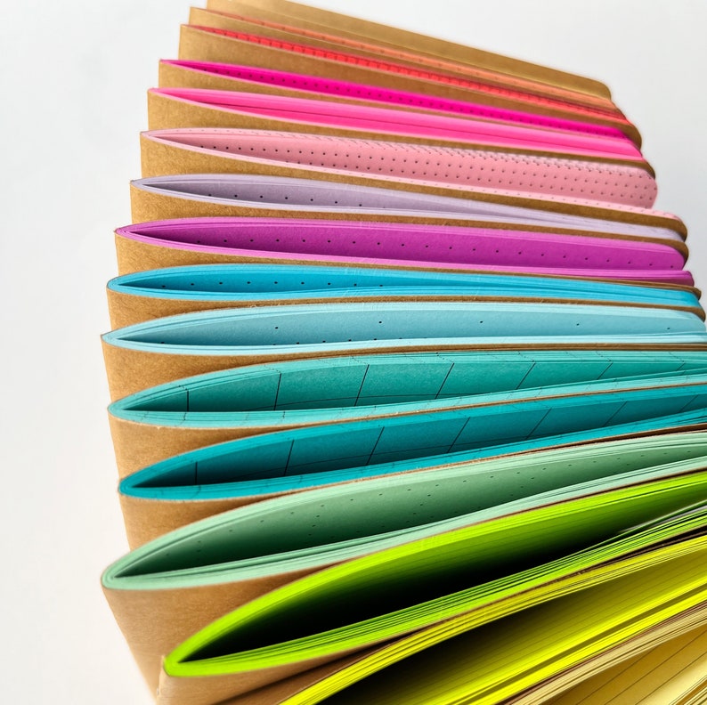 May include: A stack of colorful notebooks with different patterned paper inside. The notebooks have brown covers and are arranged in a rainbow pattern.