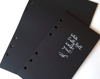 May include: Two black sheets of paper with holes punched along the side. The top sheet is slightly larger than the bottom sheet. The bottom sheet has white text that says "white Gelly Roll works great!"