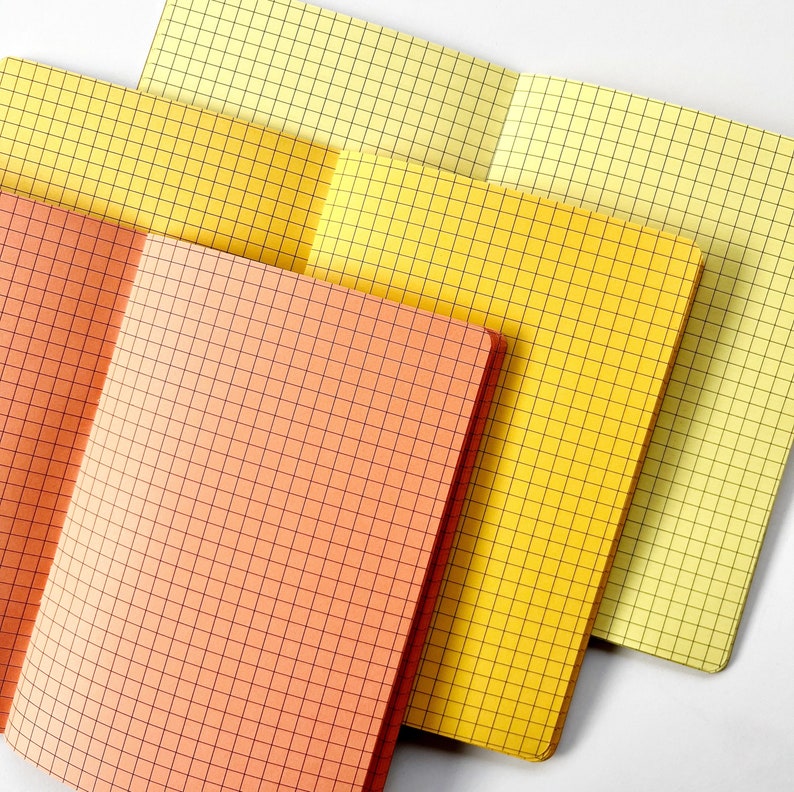 May include: Four notebooks with grid paper. The top notebook is yellow, the next two are yellow with a slight orange tint, and the bottom notebook is orange.