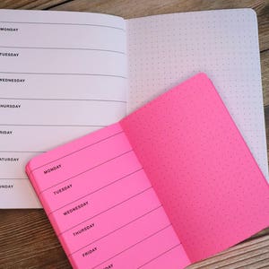 Puede incluir: Un cuaderno rosa y blanco con un patr&oacute;n de puntos en un lado y una p&aacute;gina rayada con los d&iacute;as de la semana en el otro lado. Los d&iacute;as de la semana son lunes, martes, mi&eacute;rcoles, jueves, viernes, s&aacute;bado y domingo.