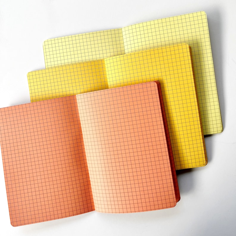 May include: Three notebooks with grid paper. The top notebook is yellow, the middle notebook is orange, and the bottom notebook is a light peach color.