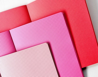 May include: Three notebooks with grid patterns. The top notebook is red, the middle notebook is pink, and the bottom notebook is a light pink.