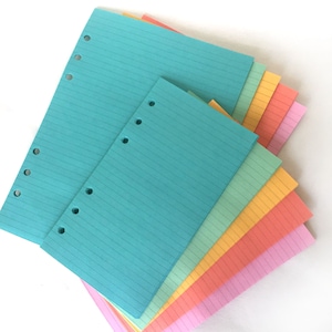 Puede incluir: Un paquete de recambios de papel rayado en varios colores pastel, incluyendo turquesa, verde claro, amarillo, naranja, rosa y morado claro. El papel tiene agujeros perforados a lo largo del lado para su uso en una carpeta.