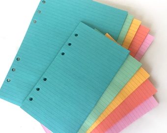 May include: A stack of lined paper refills in various pastel colors, including turquoise, light green, yellow, orange, pink, and light purple. The paper has holes punched along the side for use in a binder.