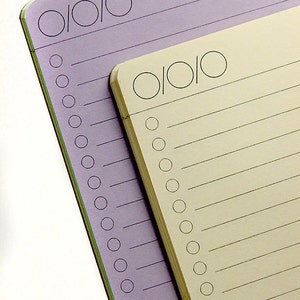 May include: Two lined notebooks, one purple and one cream, with a row of circles at the top of each page.