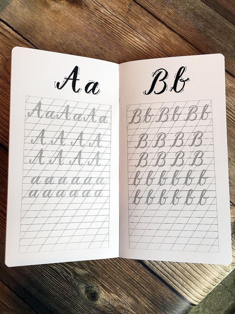 May include: An open notebook with lined pages for practising calligraphy. The letters "Aa" and "Bb" are written in large, bold script at the top of each page. The letters are repeated in smaller script on the lined pages.