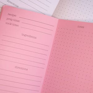 Puede incluir: Diario de recetas rosa abierto, que revela páginas rayadas para detalles de recetas y páginas punteadas para notas. El diario incluye indicaciones para la receta, el tiempo de preparación, el tiempo de cocción, los ingredientes y las instrucciones.