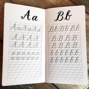 Puede incluir: Un cuaderno abierto con p&aacute;ginas rayadas para practicar caligraf&iacute;a. Las letras "Aa" y "Bb" est&aacute;n escritas en letras grandes y en negrita en la parte superior de cada p&aacute;gina. Las letras se repiten en letras m&aacute;s peque&ntilde;as en las p&aacute;ginas rayadas.
