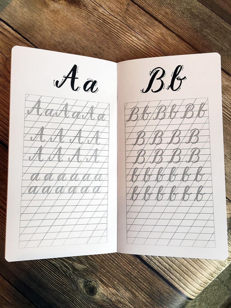 Puede incluir: Un cuaderno abierto con p&aacute;ginas rayadas para practicar caligraf&iacute;a. Las letras "Aa" y "Bb" est&aacute;n escritas en letras grandes y en negrita en la parte superior de cada p&aacute;gina. Las letras se repiten en letras m&aacute;s peque&ntilde;as en las p&aacute;ginas rayadas.
