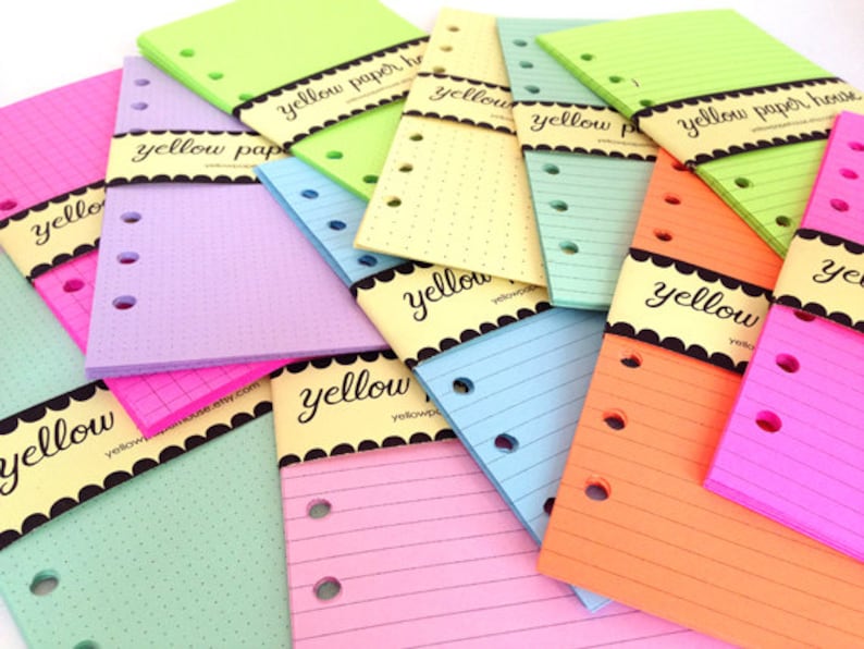 May include: A stack of colorful, hole-punched paper refills for a planner or notebook. The paper is in various colors, including green, pink, blue, and orange. The paper is labeled with the text "yellow paper house".