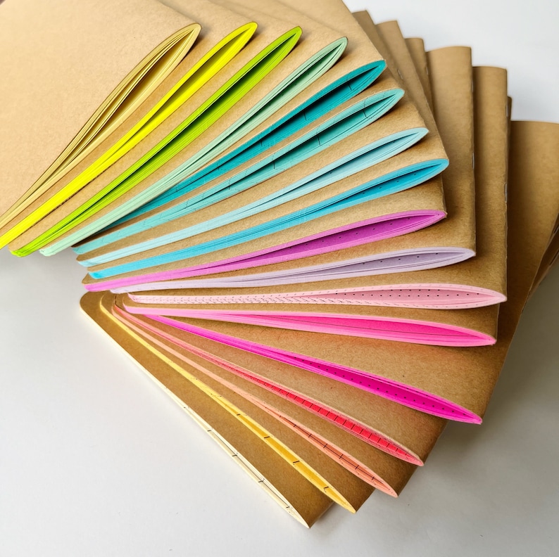 May include: A stack of brown notebooks with colorful edges. The notebooks are fanned out in a rainbow pattern, with each edge a different color. The notebooks are all the same size and shape.