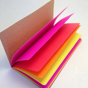May include: A small notebook with a brown paper cover and brightly colored pages. The pages are pink, red, orange, and yellow. The notebook is open and the pages are fanned out.