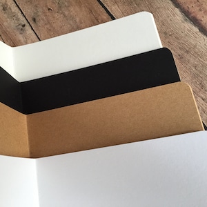 May include: A stack of four sheets of paper in different colors. The top sheet is white, the second sheet is black, the third sheet is brown, and the bottom sheet is white.