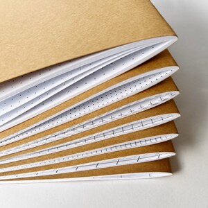 May include: A stack of notebooks with different paper styles. The top notebook has a brown cover and the others have white covers with different patterns.