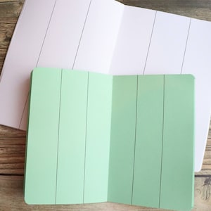 May include: Two notebooks, one with a white cover and the other with a green cover. Both notebooks have vertical lines on the pages.