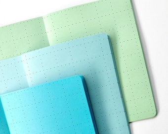 May include: Three notebooks with dotted pages, one is light green, one is light blue, and one is a darker blue.