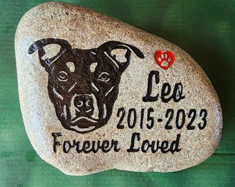 May include: A memorial stone with a carved dog portrait and the name "Leo" along with the years 2015-2023. A red heart with a paw print is next to the name. The words "Forever Loved" are also carved into the stone.