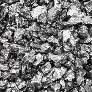 May include: Close-up of a pile of irregularly shaped, metallic gray stones. The stones have a rough, textured surface and varying sizes, creating a dense, uneven pattern. The lighting highlights the reflective qualities of the material.