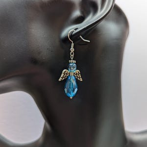 Puede incluir: Pendientes de aro de plata con alas de &aacute;ngel y un cristal azul en forma de l&aacute;grima.