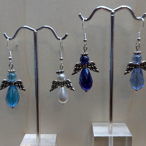 Puede incluir: Tres pares de pendientes colgantes con forma de &aacute;ngel. Un par presenta un cristal azul, otro una perla blanca y el tercero un cristal azul oscuro.
