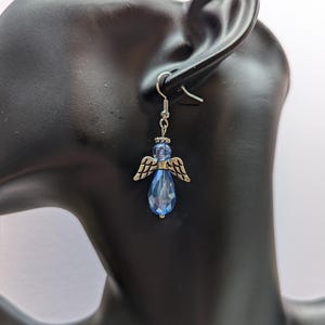 Puede incluir: Pendientes de plata con alas de &aacute;ngel y un colgante de cristal azul en forma de l&aacute;grima.