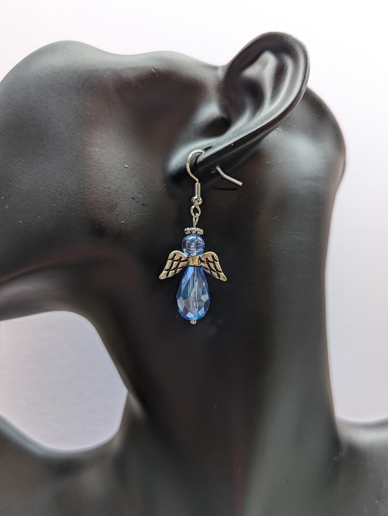 Puede incluir: Pendientes de plata con alas de &aacute;ngel y un colgante de cristal azul en forma de l&aacute;grima.