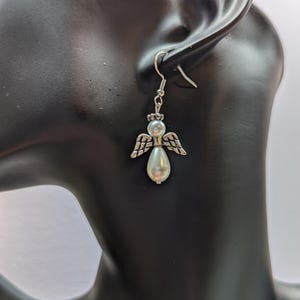 Puede incluir: Pendientes de plata con forma de &aacute;ngel y una perla blanca. Los pendientes est&aacute;n en la oreja de un maniqu&iacute;.