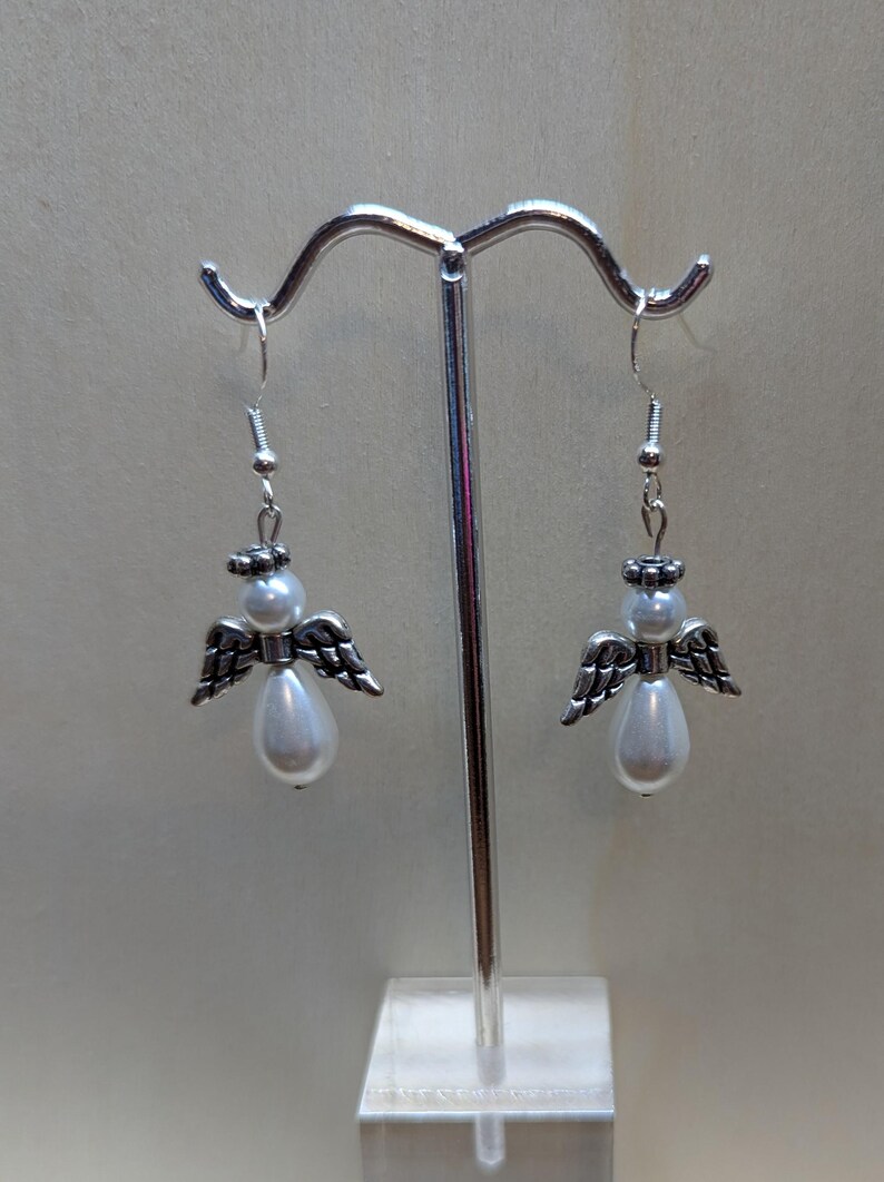 Puede incluir: Un par de pendientes de &aacute;ngel colgantes de plata con detalles de perlas blancas.