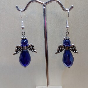 Puede incluir: Un par de pendientes colgantes con una l&aacute;grima de cristal azul y alas de &aacute;ngel plateadas.