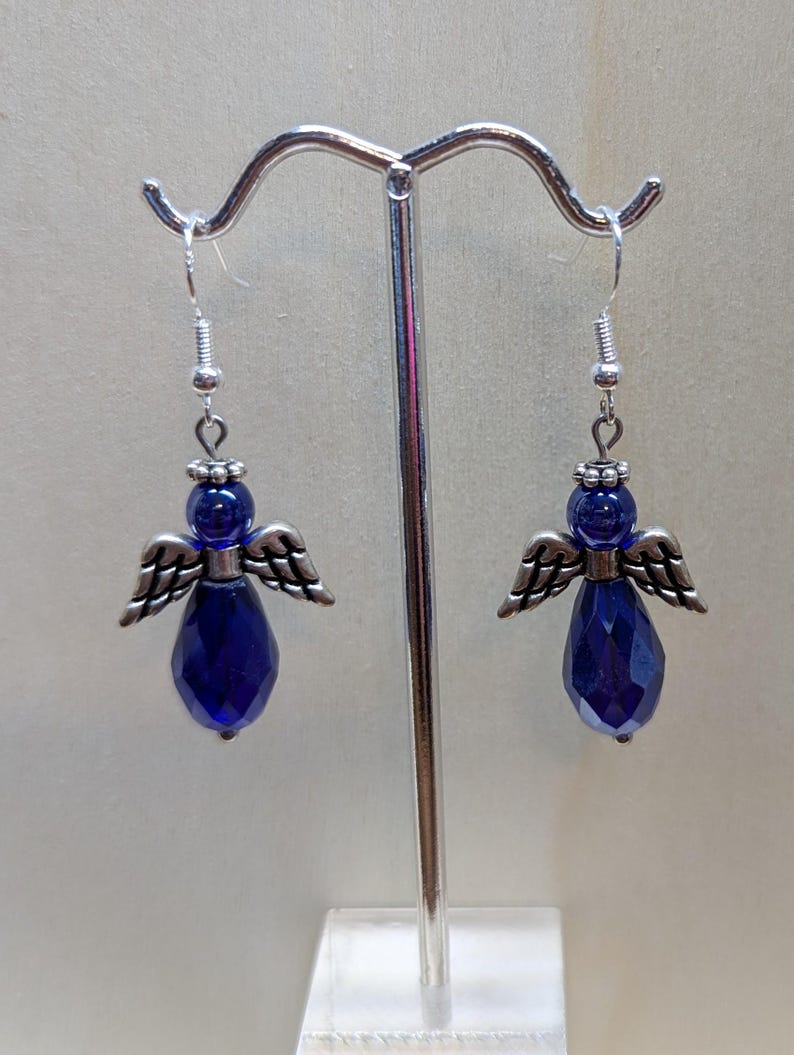 Puede incluir: Un par de pendientes colgantes con una l&aacute;grima de cristal azul y alas de &aacute;ngel plateadas.