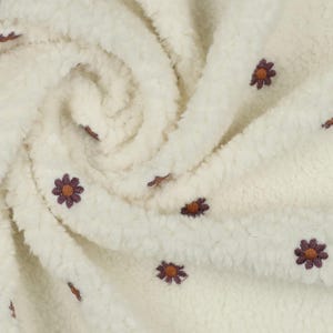 Könnte beinhalten: Weißer Kunstpelzstoff mit einer dezenten Textur und kleinen, gestickten braunen Blumen.