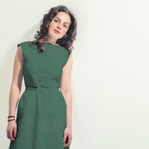 May include: A woman wearing a green sleeveless dress with a belt. The dress has a simple, classic design.