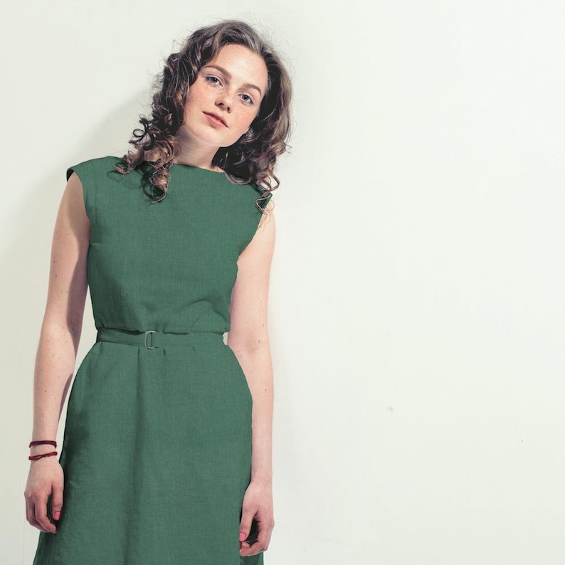 May include: A woman wearing a green sleeveless dress with a belt. The dress has a simple, classic design.