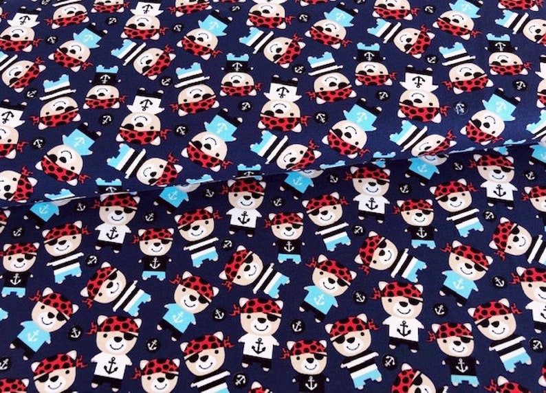 May include: Navy blue fabric with a repeating pattern of cartoon pirate bears. The bears wear red bandanas, eye patches, and sailor hats. Some bears have anchors on their shirts. The fabric is suitable for children's apparel and nautical-themed crafts.