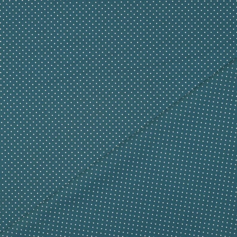 Op de afbeelding: Een teal stof met een wit stippenpatroon. De stof is doormidden gevouwen, waardoor een diagonale lijn ontstaat.