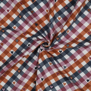 Könnte beinhalten: Ein weißer Stoff mit einem braunen, rosa und blauen Karomuster. Kleine schwarze Herzen sind über den gesamten Stoff verteilt.