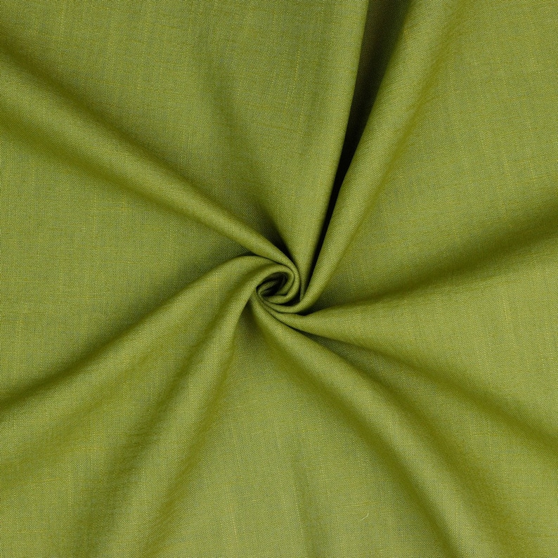 May include: A close-up of a piece of green fabric with a textured weave. The fabric is folded and draped, creating soft folds and wrinkles.