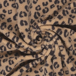 May include: Close-up of a beige fabric with a brown leopard print. The fabric is soft and fluffy, with a fuzzy texture.