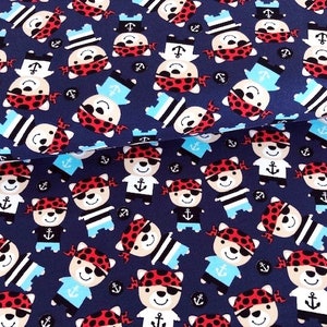 May include: Navy blue fabric with a repeating pattern of cartoon pirate bears wearing red bandanas, eye patches, and sailor hats. The bears are interspersed with anchors and sailor shirts in light blue and black.