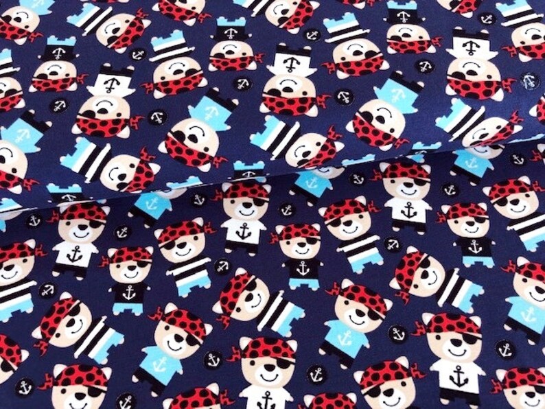 May include: Navy blue fabric with a repeating pattern of cartoon pirate bears wearing red bandanas, eye patches, and sailor hats. The bears are interspersed with anchors and sailor shirts in light blue and black.