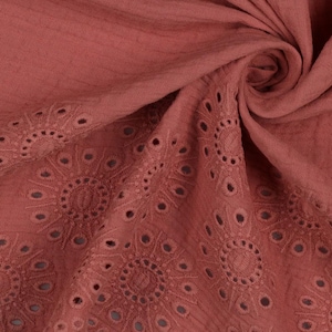 May include: Close-up of a rust-coloured fabric with a delicate eyelet pattern. The fabric is soft and textured, with a subtle sheen.