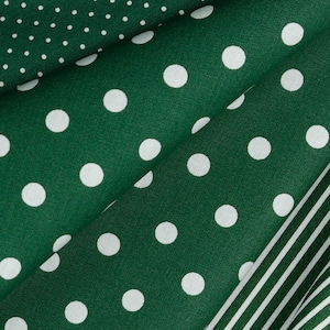 Op de afbeelding: Close-up van gevouwen groene stof met witte stippen van verschillende grootte. Een gedeelte van de stof met witte strepen is ook zichtbaar. De stof heeft een diepe bosgroene kleur en de witte stippen en strepen creëren een contrasterend patroon.