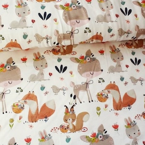 Può includere: Tessuto bianco con un motivo ripetitivo di cervi marroni con fasce floreali, volpi arancioni, conigli marroni e scoiattoli marroni. Gli animali tengono cesti di fiori e sono circondati da piccoli fiori e foglie.