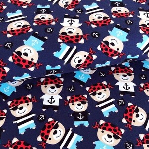 May include: Navy blue fabric with a repeating pattern of cartoon bear pirates wearing red bandanas, eye patches, and sailor hats. The bears have anchor designs on their shirts and are interspersed with anchor icons.